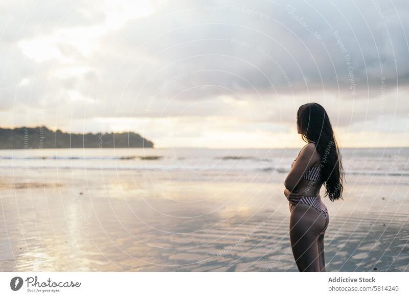 Young woman watching sunset standing on the beach young sea summer lifestyle happy travel beautiful ocean nature vacation people sky female happiness outdoor