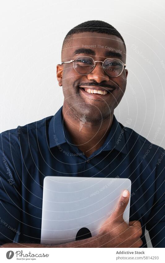 Smiling black guy with laptop near white wall man netbook happy well dressed contemporary positive eyeglasses studio shot smile african american arms crossed