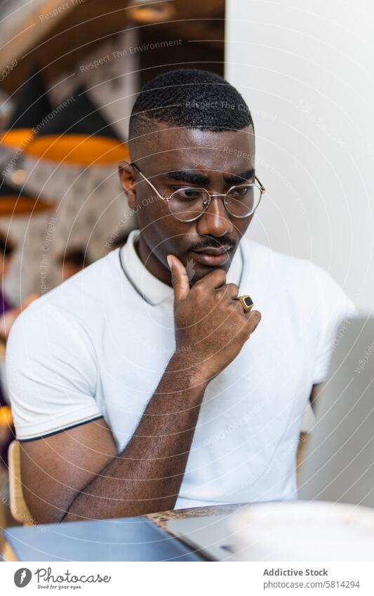 Serious African American man using laptop at table in cafe thoughtful cup drink eyeglasses modern serious african american black male adult online computer