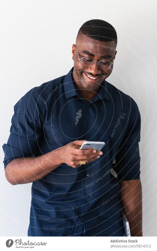 Happy black guy with phone and laptop near white wall man smartphone well dressed modern eyeglasses studio shot netbook african american male adult shirt