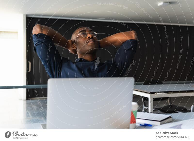 Black man taking break from work near laptop in office table thoughtful takeaway drink notepad document modern african american black male adult chair paper cup