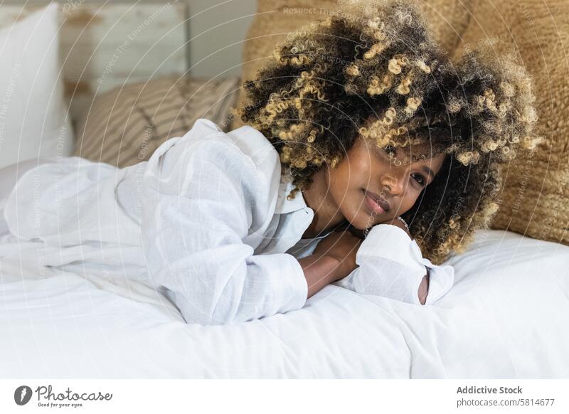 Thoughtful black woman lying on bed in bedroom enjoy rest positive comfort relax morning female happy home glad carefree hairstyle ethnic african american