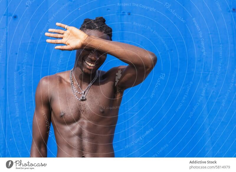 Muscular black man with naked torso muscular shirtless portrait toothy smile strong shy hiding chain fit masculine physical young african american ethnic male