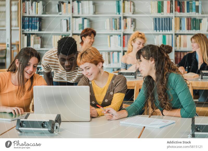 Diverse students discussing data on laptop project analyze library together smile education study teen teenager adolescent young university group research