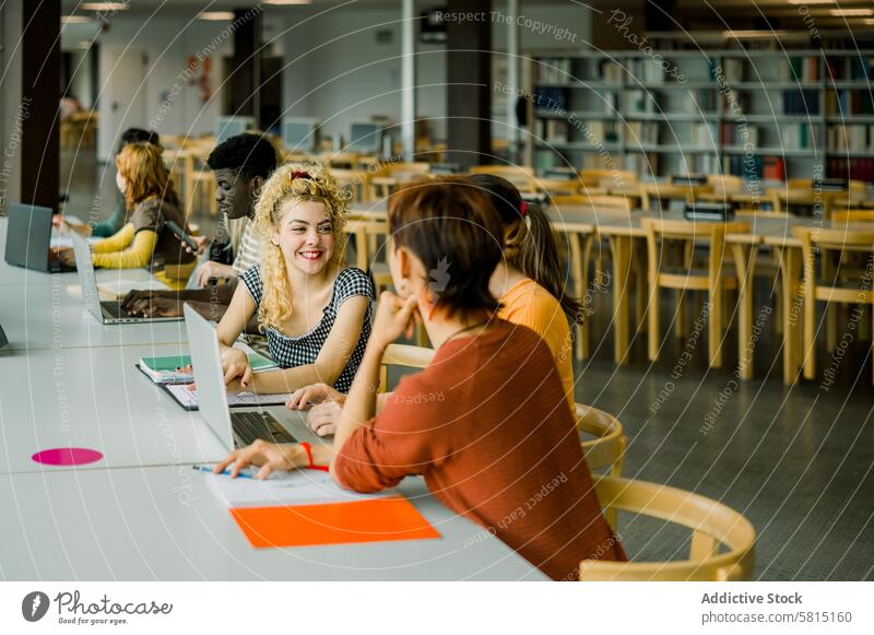 Group of multiethnic students sitting in library group men women conversation discuss collaborate study interact laptop smile teamwork communicate diverse