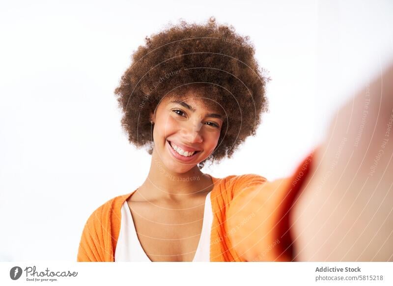 young latina woman with afro hair smiling takes a self-portrait studio isolated white background jacket orange color smile female happy person lifestyle