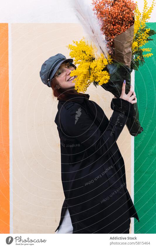 Woman with flowers smiling against colorful wall woman smile street style happy bouquet pavement carry female young urban outerwear season delight bunch town