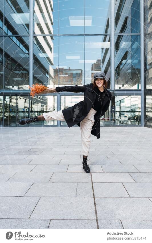 Happy woman with flowers dancing on street dance smile bouquet glass wall building downtown style female happy pavement modern leg raised cheerful urban glad