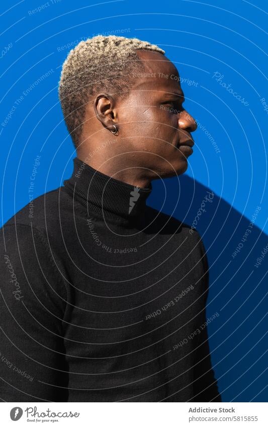 Serious black guy standing against blue wall in sunlight man calm pensive serious style street chill bright relax thoughtful confident male young