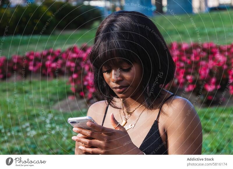 Thoughtful young black woman messaging on smartphone serious using texting message social media gadget browsing connection female internet cellphone park