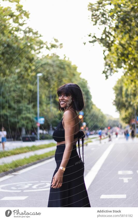 Positive stylish black woman in green park happy cheerful elegant toothy smile delight charming positive glad female content optimist walkway dress young trendy