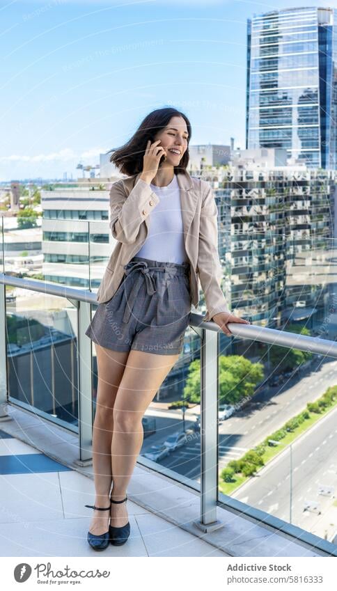 A woman is taking a break from work and chatting on her cell phone while standing on a balcony Modern attractive background beauty business businesswoman call