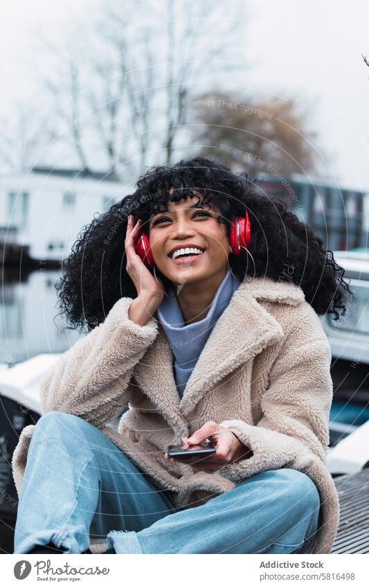 Cheerful black woman listening to music at lakeside headphones smartphone using chill rest relax park female african american woman city smile positive urban