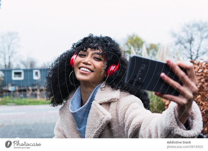 Black woman taking selfie on street smartphone headphones using music listen chill female african american woman black woman city portrait smile positive autumn