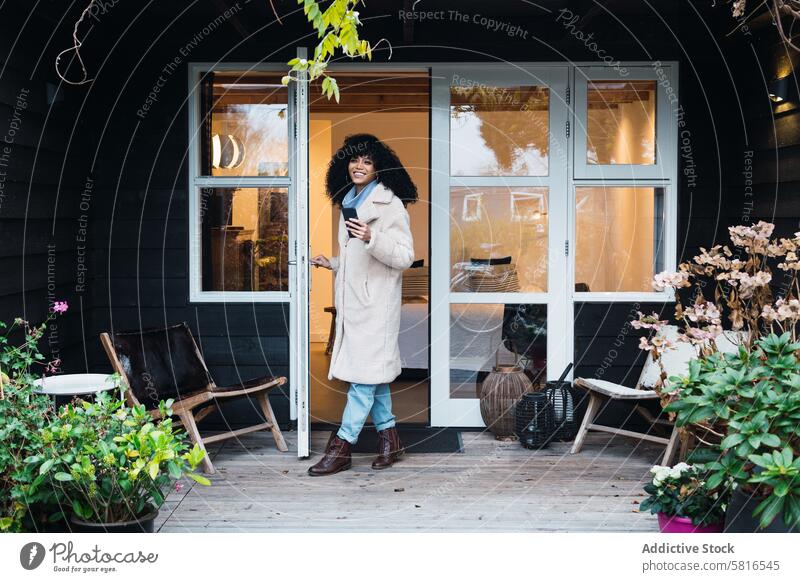 Happy black woman standing in doorway of house home walking out warm clothes coat outerwear urban smartphone female african american woman personality entrance