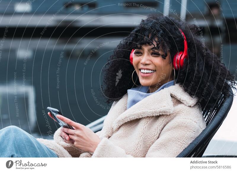 Cheerful black woman listening to music at lakeside headphones smartphone using chill rest relax park female african american woman city smile positive urban