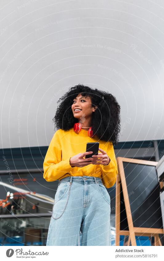 Cheerful stylish ethnic lady standing and using smartphone in contemporary building woman smile communicate confident trendy positive happy staircase message