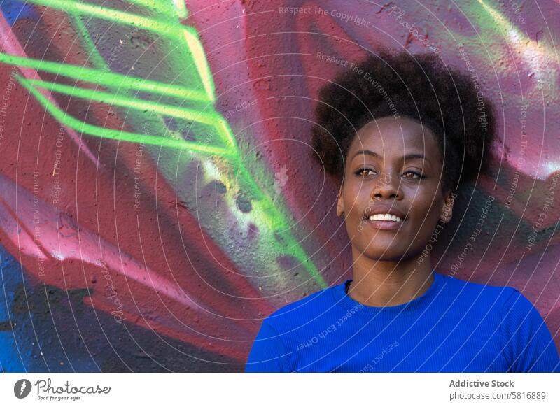 Black woman standing near wall with graffiti city lean relax urban cool street art smile female ethnic black african american colorful creative curly hair happy