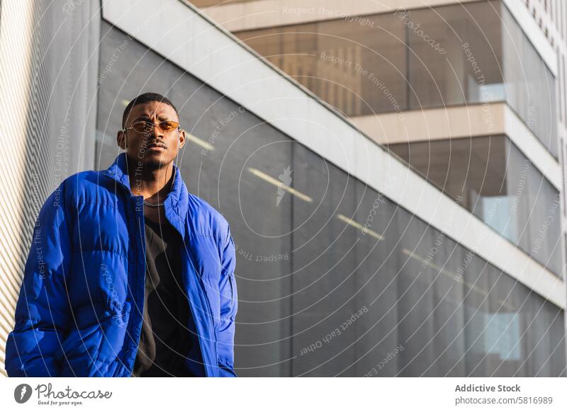 Stylish black man in sunglasses on street style orange trendy outfit determine cool urban male ethnic metal wall african american confident modern warm jacket