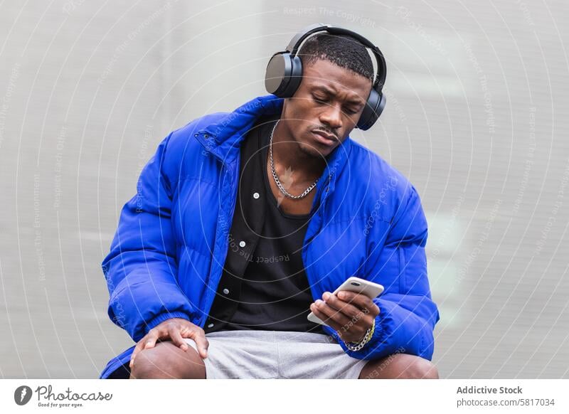 Black man with headphones on smartphone in city listen music calm song wireless street male ethnic black african american jacket young audio peaceful hobby