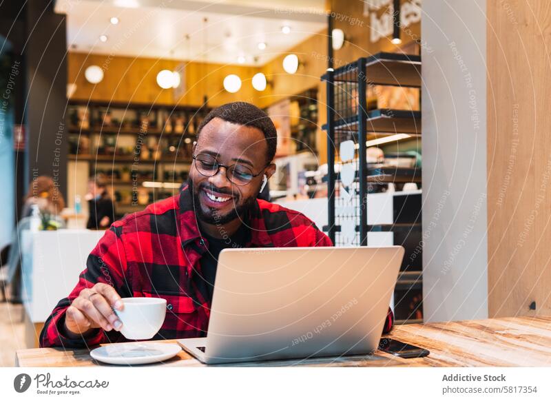 Smiling black man working on laptop in cafe earphones using online internet browsing freelance male african american netbook surfing coffee remote connection