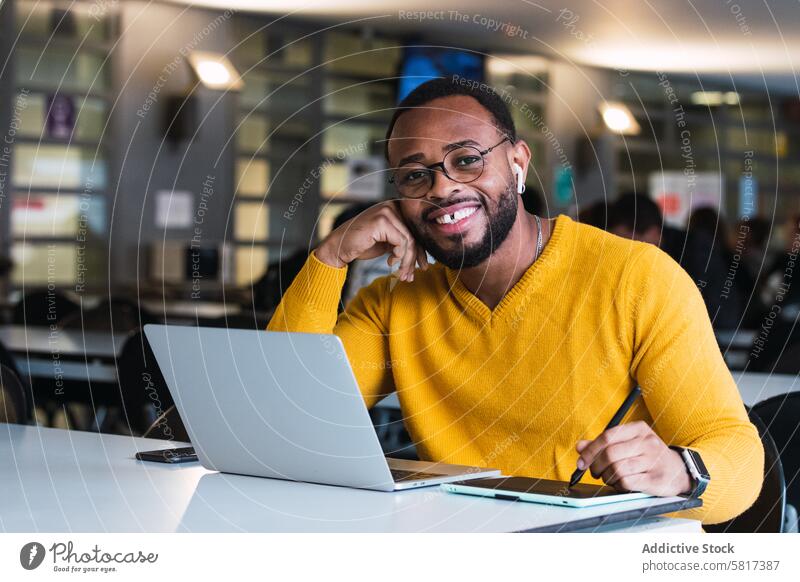 Smiling black man working on laptop with tablet graphic tablet designer earphones using online internet office take note male african american netbook