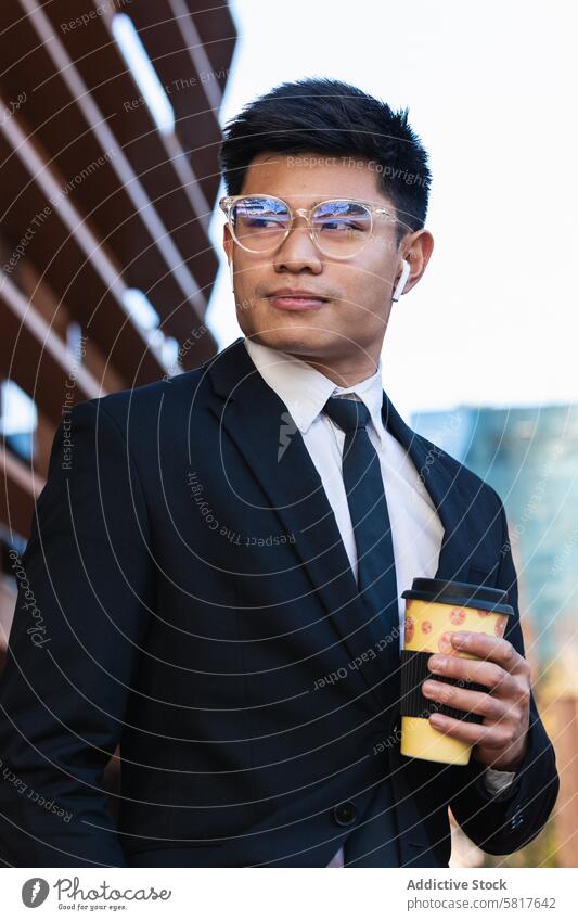 Handsome ethnic businessman with takeaway coffee in city handsome suit entrepreneur to go masculine street male asian wireless earbuds beverage drink paper cup