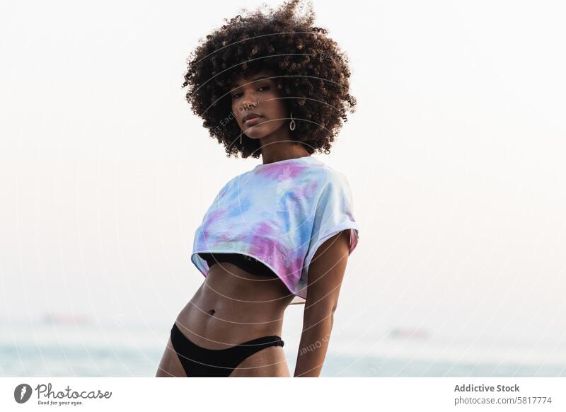 Unemotional black woman standing on seashore bikini summer holiday crop top vacation female ethnic african american panties curly hair afro hairstyle relax