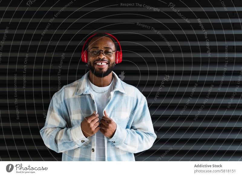 Smiling black man in headphones and jacket meloman music cheerful street song city wall stylish smile african american happy male guy style trendy building