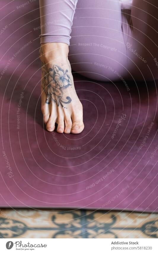 Crop foot of tattooed woman in sports clothes barefoot floor ornament creative design sportswear wellness house decorative leggings tiptoe wellbeing vitality