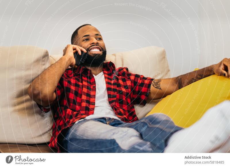 African american man making a call with smartphone relaxed at home sofa black couch african american mobile technology happy communication cheerful adult