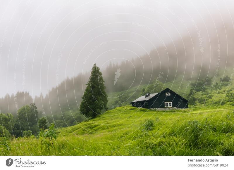 Isolated house in the mountains, beautiful typical northern European house in a lush, green landscape with fog. Beautiful summer landscape with green meadows and house in the mountains.