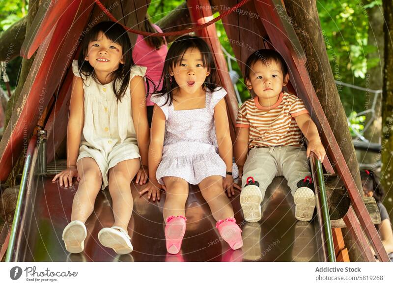 Asian siblings enjoying a slide in a European playground child park vacation europe family fun outdoor asian laughter playful summer travel adventure leisure