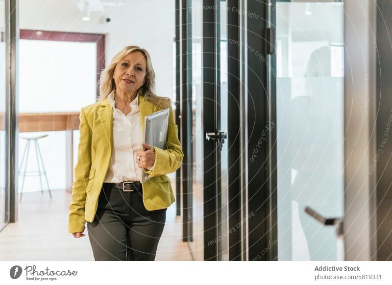 Professional woman walking through coworking office space professional businesswoman modern leadership confident stylish corporate documents jacket bright