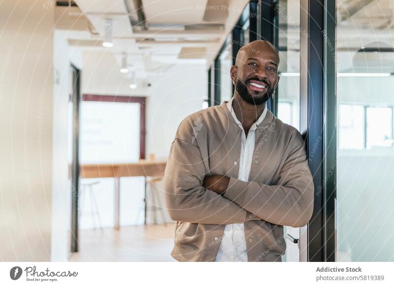 Confident businessman in modern coworking space confident smiling standing arms crossed office professional approachable well-lit workspace entrepreneur startup