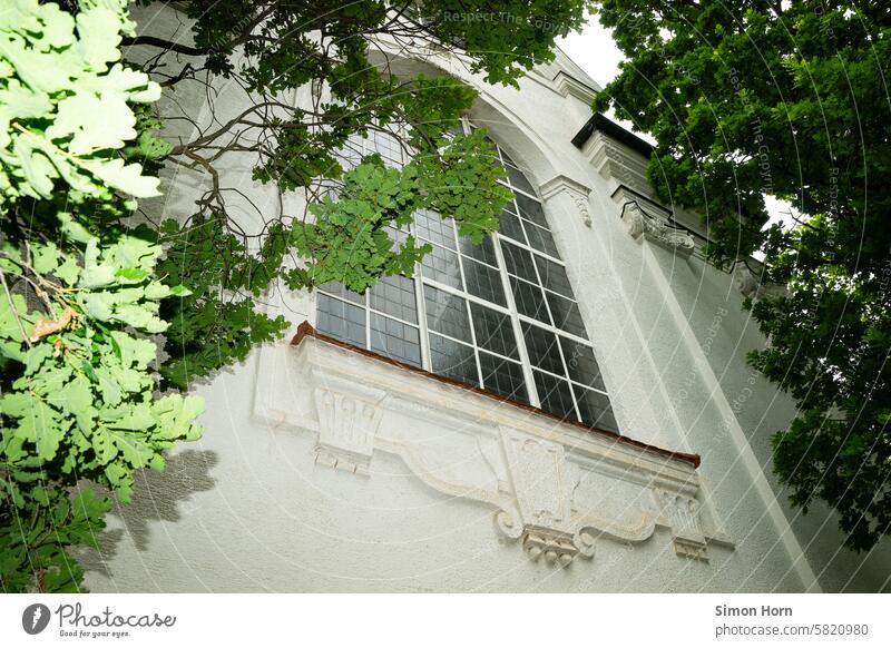 large window of a church between the green leaves of large trees Church Church window framed city view City church sacral building Window Religion and faith