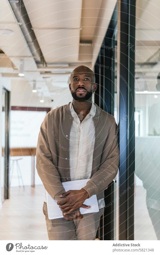 Professional man standing in modern coworking space business professional office stylish contemplative dressed well-dressed black documents office space worker