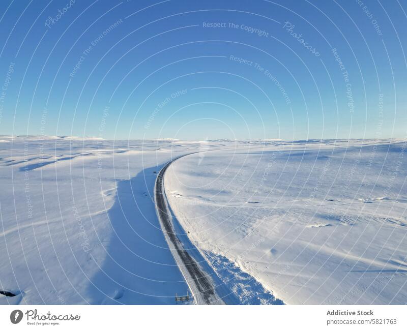 Winding road amidst expansive snowy landscape in Iceland iceland aerial view solitude nature winter clear sky blue cold arctic outdoor travel beauty panoramic