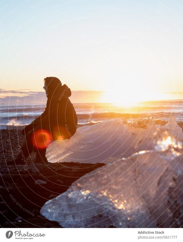 Silhouetted figure contemplating by a sunlit Icelandic shore iceland silhouette sunset beach contemplation nature serenity solitude ocean evening sunlight