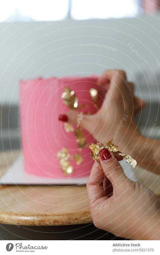 Decorating a Pink Cake with Gold Leaf Accents cake decoration gold leaf pink baking pastry art frosting dessert hand close-up confectionery creativity kitchen