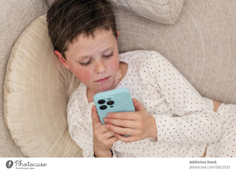 Boy Engrossed in Smartphone at Home boy child kid home smartphone lying down couch focused indoors technology casual relaxation leisure screen time