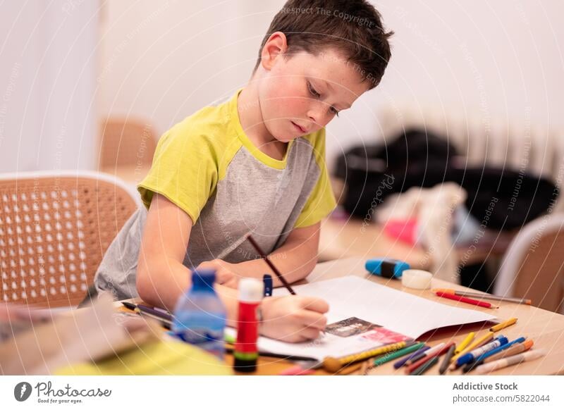 Boy focused on drawing at home boy child creativity colored pencils artwork looking down indoor concentration leisure hobby table sitting casual education