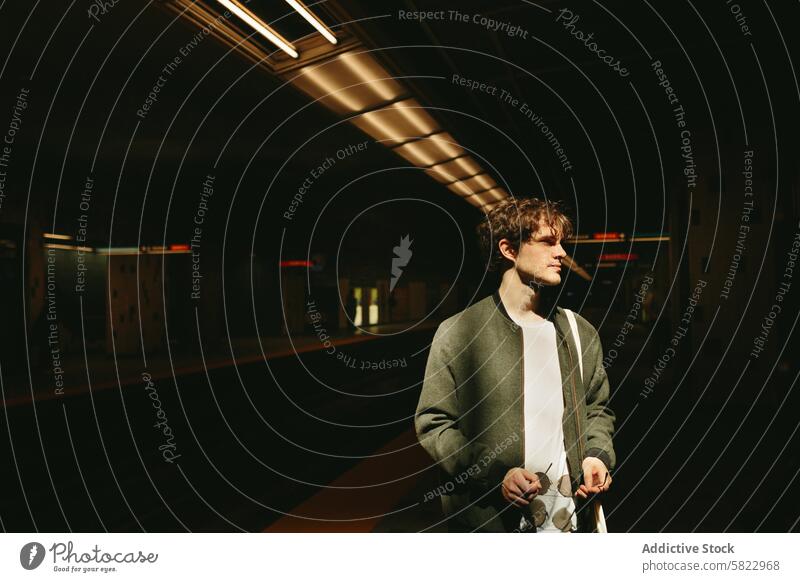 Young man standing alone in an empty subway station young reflective contemplative urban sunlight glow casual attire thoughtful male adult warm basking filter