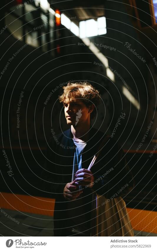 Young man in moody urban stairwell with sunlight shadow introspection young contrast deep thought dynamic casual clothing holding bag indoor architecture modern