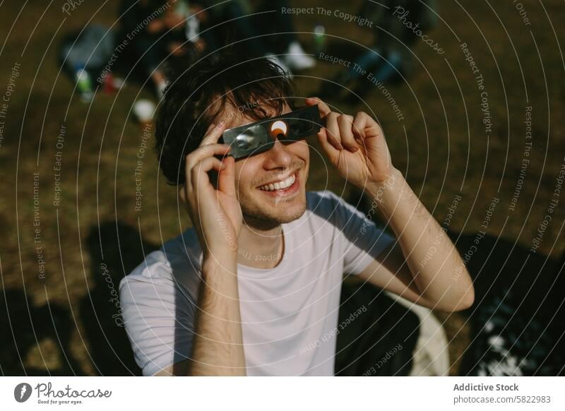 Young man using binoculars in a sunny park young grass outdoor friends day leisure nature smile happy cheerful male youthful casual relax recreation picnic