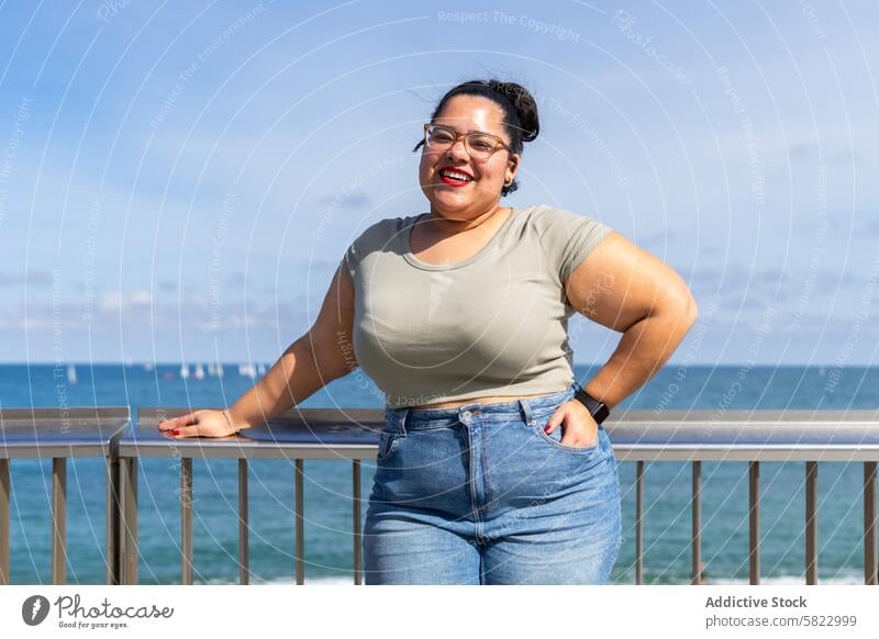 Smiling woman enjoying summer by the Barcelona shore smile barcelona sea sky casual railing leaning coast beach cheerful joyful sunny ocean plus size glasses