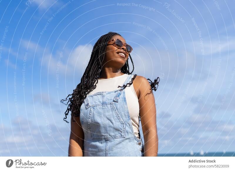 Smiling woman enjoying summer in Barcelona barcelona sky smile denim jumpsuit carefree spirit sunglasses blue sky clear sky happiness sunny outdoors youth