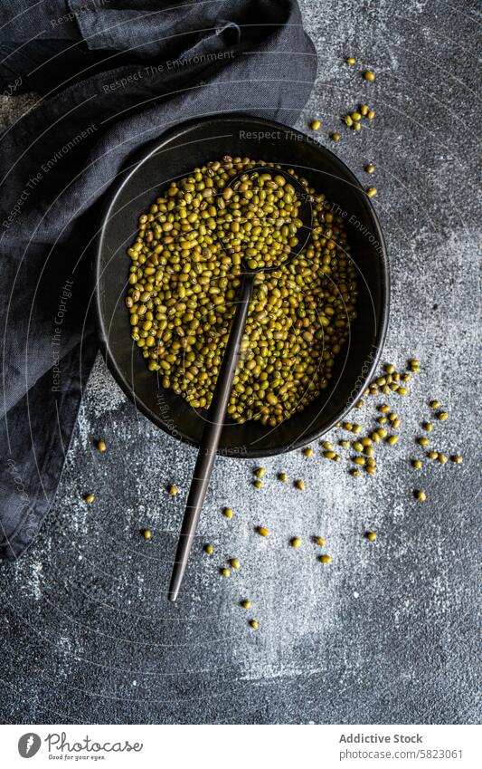 **Bowl of raw green mung beans with a spoon, dark backdrop** organic bowl metal textured surface grey rustic food legume uncooked natural healthy nutrition