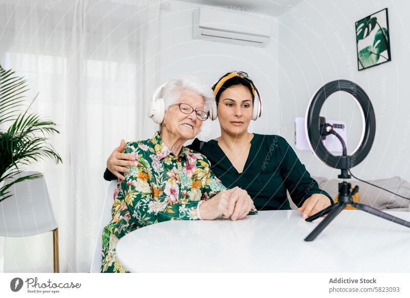 Young and elderly woman recording a podcast together young adult headphones ring light smartphone modern home bright technology media communication interaction