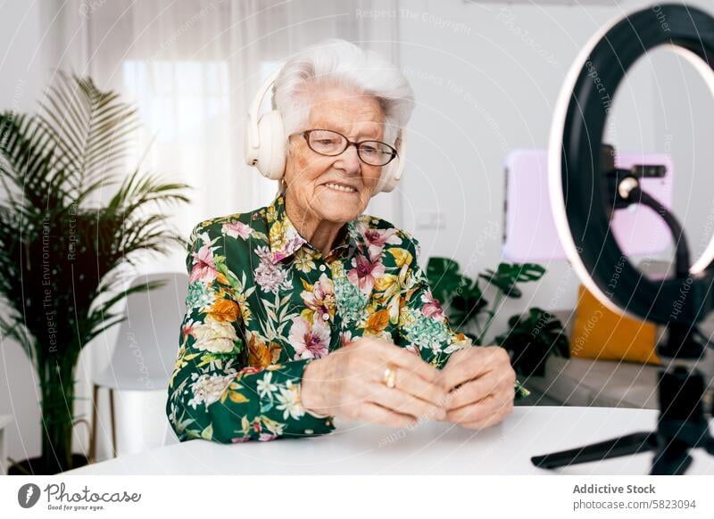 Elderly woman recording creative podcast at home elderly video social media influencer joyful audience headphones shirt floral technology content creator senior